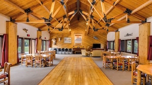 A spacious dining area with wooden tables and chairs, a high wooden ceiling with trusses, and large windows with curtains. - Blue Mesa Recreational Ranch (Gunnison)
