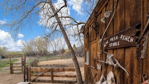 A rustic wooden building labeled "Blue Mesa Ranch Stable" with a wooden fence and a tree in the foreground. - Blue Mesa Recreational Ranch (Gunnison)