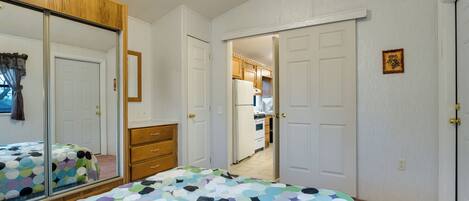 Un dormitorio con cama, un espejo grande, un armario y una puerta que da a una cocina.