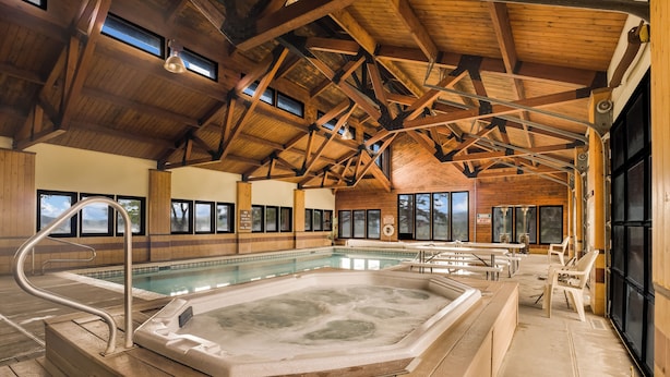 A large indoor swimming pool with a hot tub, wooden beams, and a view of the outdoors. - Blue Mesa Recreational Ranch (Gunnison)