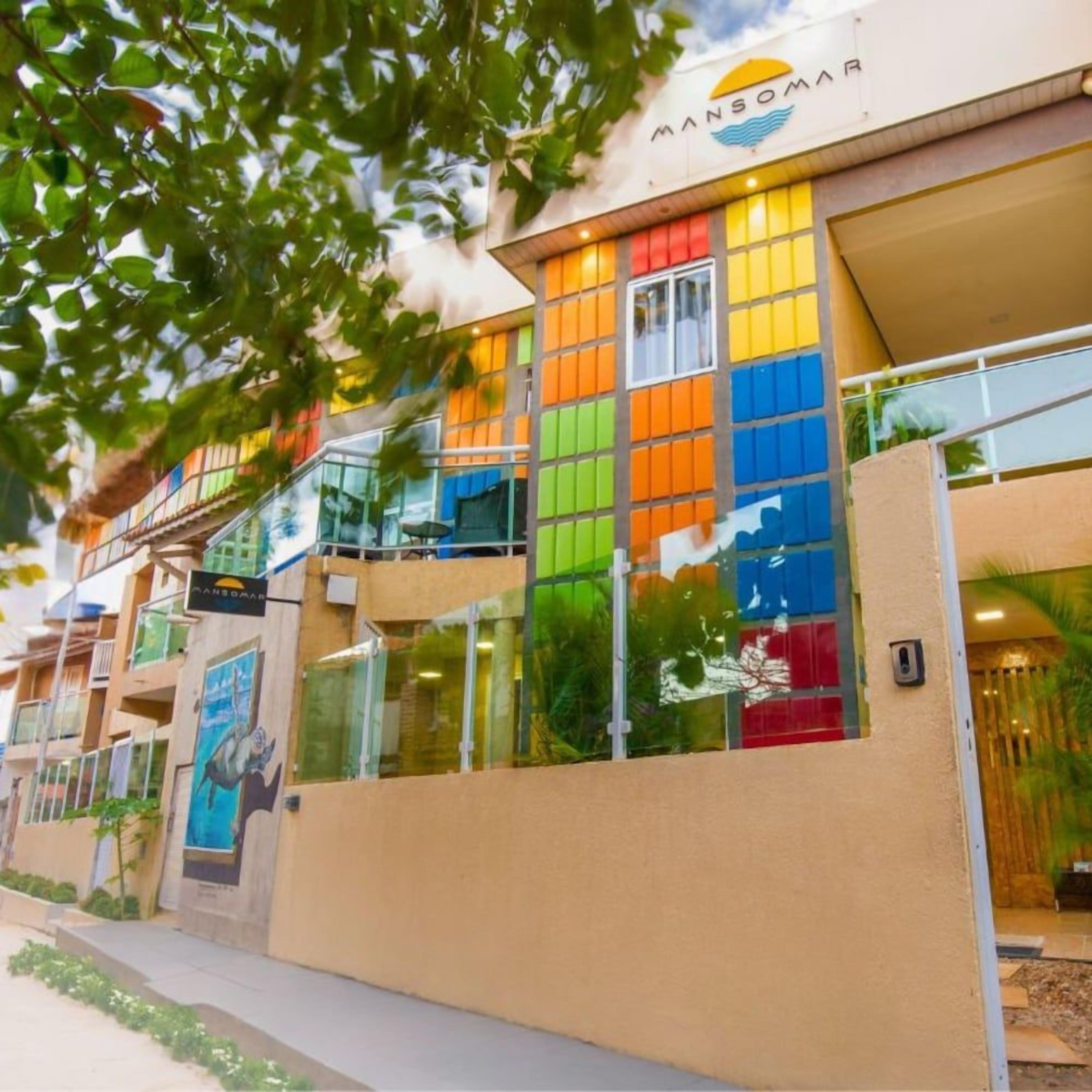 Um edifício com fachada colorida, uma placa visível com a inscrição 'MANSOMAR' e entrada de vidro.