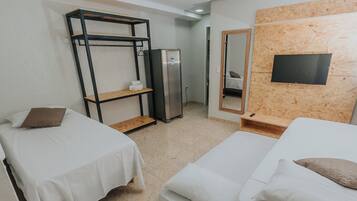 Ein Hotelzimmer mit zwei Einzelbetten, einem Kleiderschrank, einem Kühlschrank, einem Spiegel und einem an einer Holzwand befestigten Fernseher.