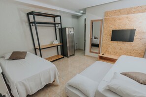 Habitación de hotel con dos camas individuales, un armario, un refrigerador, un espejo y un televisor fijado en una pared de madera.