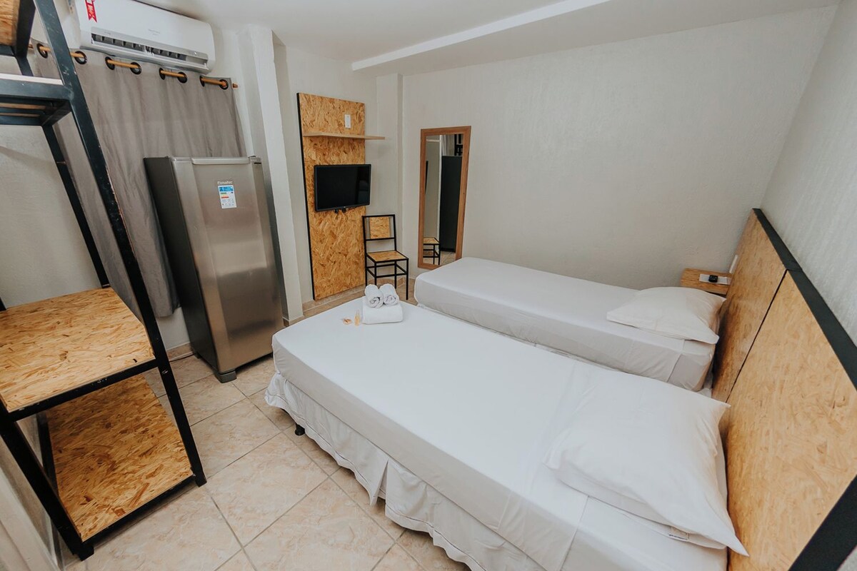 A hotel room with two beds, a refrigerator, a TV, and a wooden shelf.