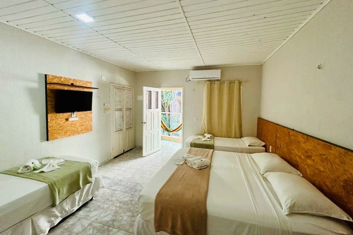 A hotel room with two beds, a television, an air conditioning unit, a window with curtains, and a door leading to a balcony.