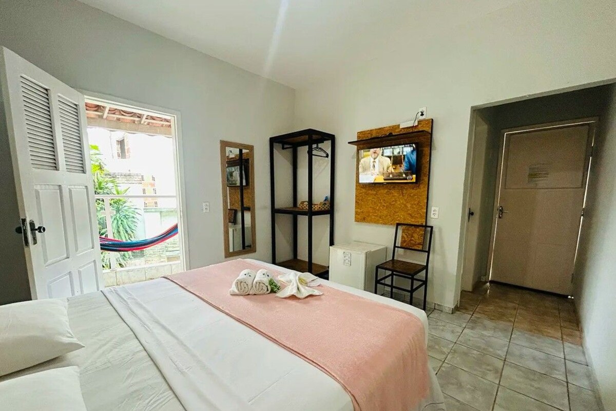 A hotel room with a bed, a TV mounted on the wall, a wardrobe, and a door leading to a balcony.