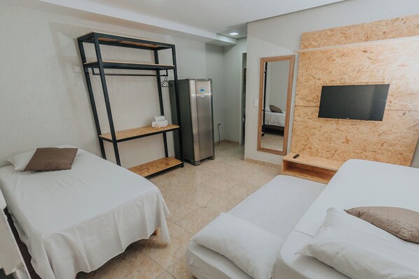 Habitación de hotel con dos camas individuales, un armario, un refrigerador, un espejo y un televisor fijado en una pared de madera.