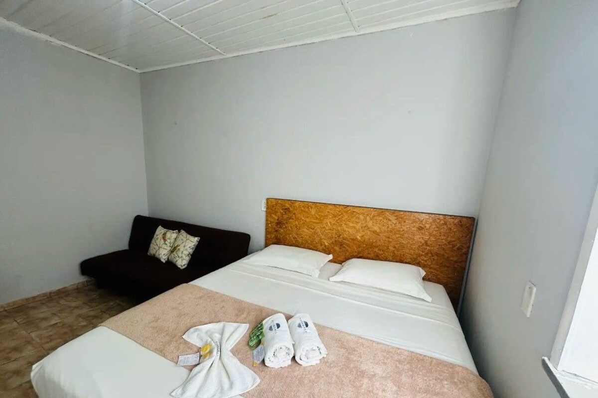 A hotel room with a bed, a dark-colored sofa, and a wooden headboard.