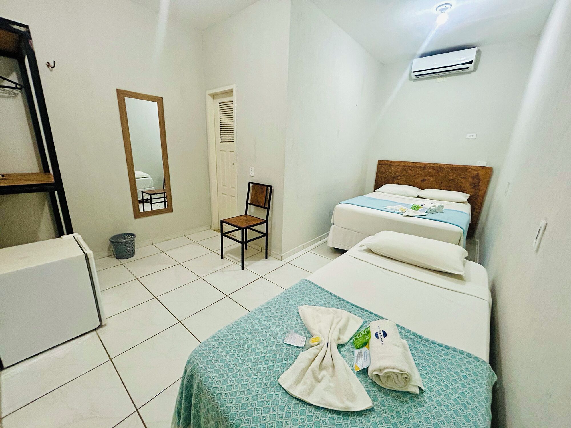 Una habitació d'hotel amb un llit, una cadira, una taula petita, un mirall i un aparell d'aire condicionat.