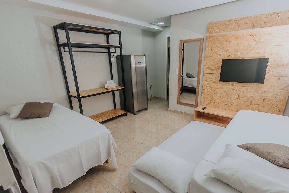 Una habitació d'hotel amb dos llits individuals, un armari, un refrigerador, un mirall i una televisió penjada a una paret de fusta.