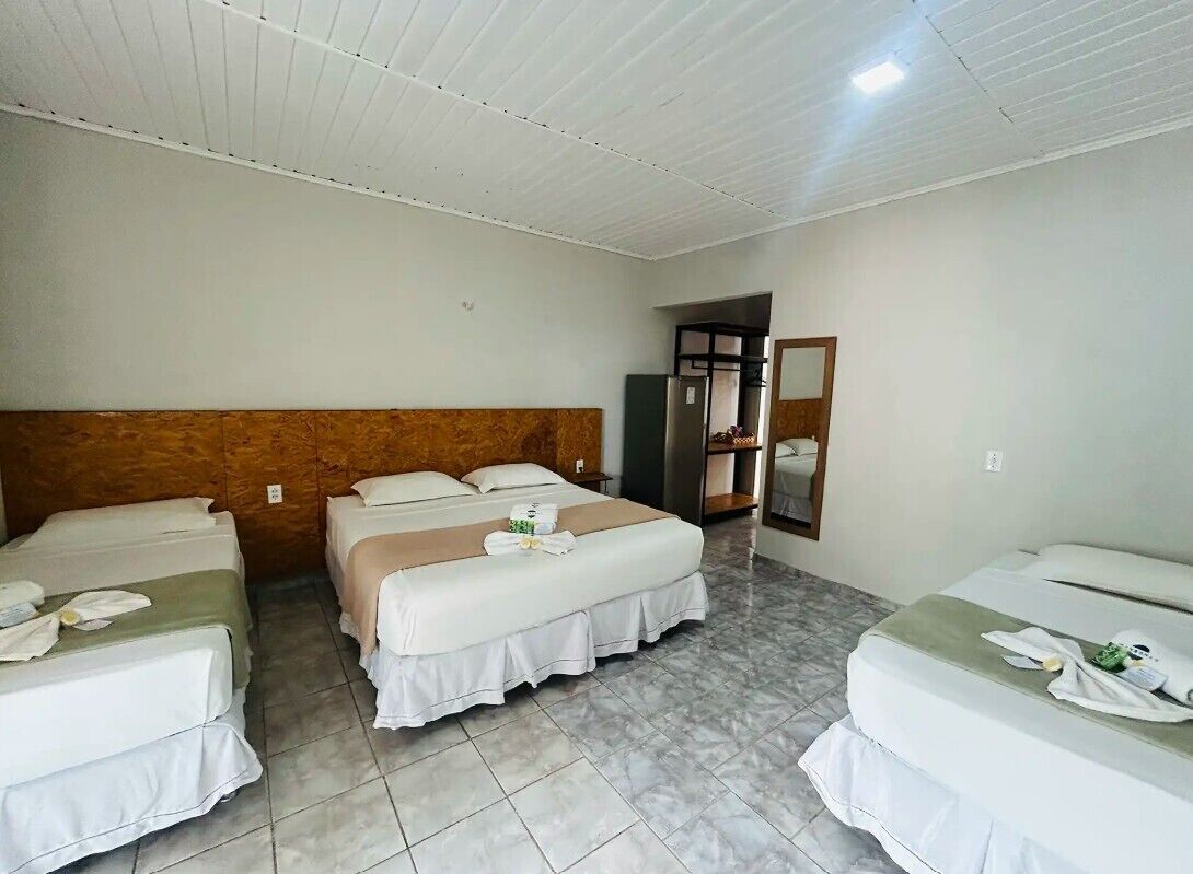 Habitació d'hotel amb tres llits, un panell de capçalera de fusta, un mirall i un terra de rajola.