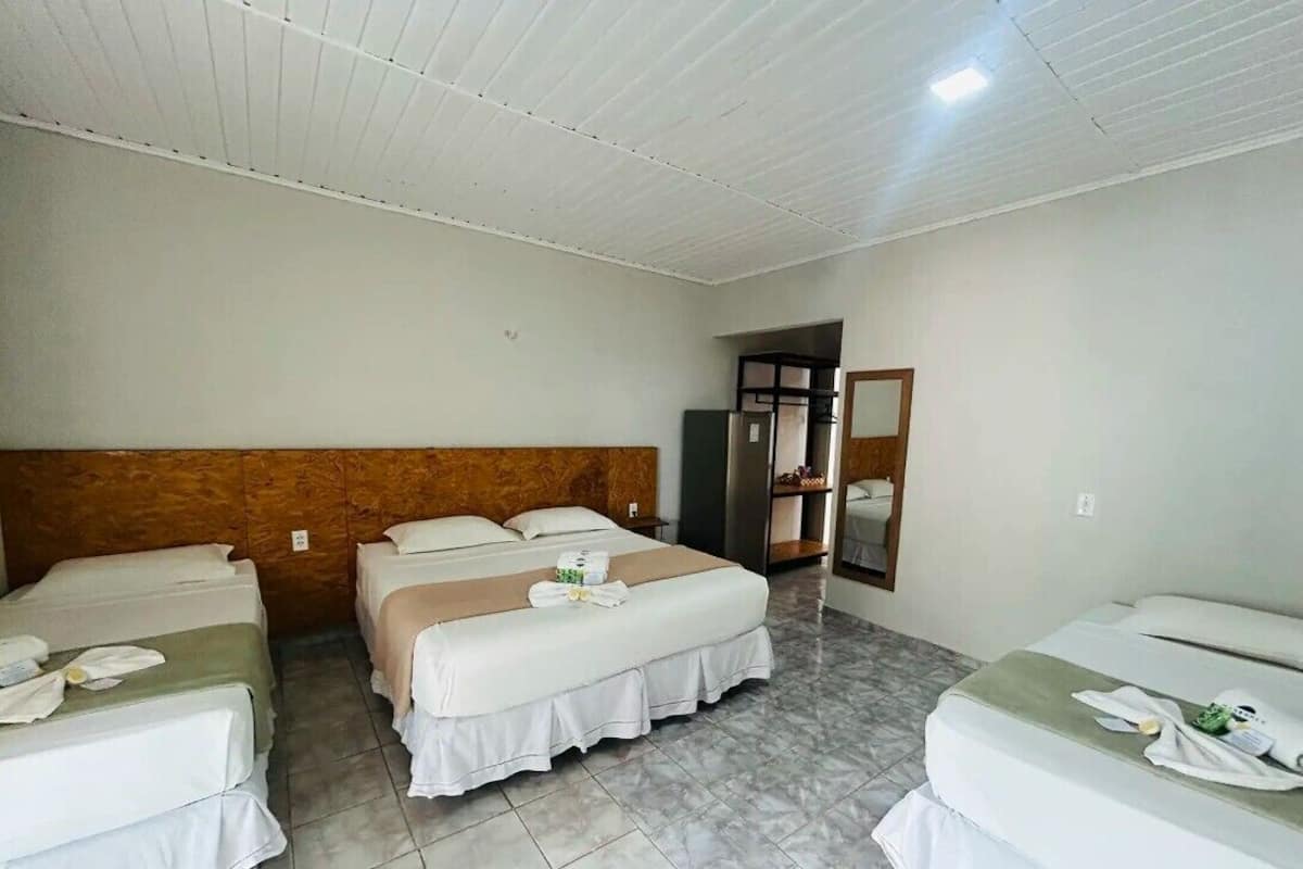 Habitació d'hotel amb tres llits, un panell de capçalera de fusta, un mirall i un terra de rajola.