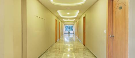 Un pasillo largo e iluminado con suelo de mármol y puertas de madera, que conduce a una habitación luminosa con un ventanal grande.