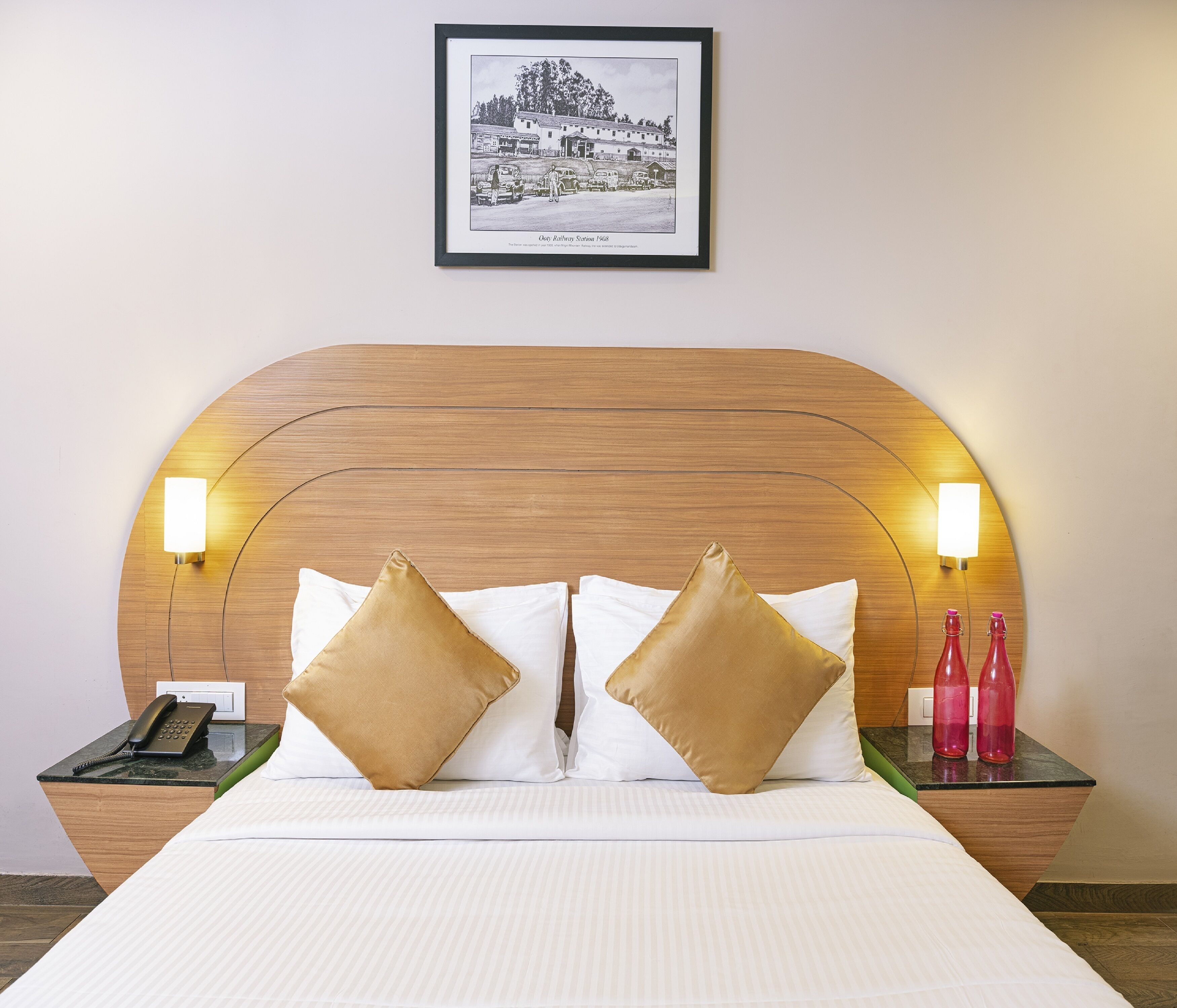 A hotel room with a large bed, two bedside tables, a framed picture on the wall, and a telephone on one of the tables.