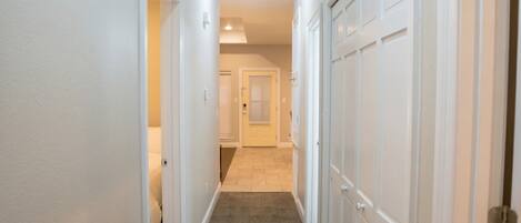 A hallway with white walls, a carpeted floor, and a door at the end.