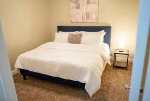 A neatly made bed with white linens, a dark headboard, and a small bedside table with a lamp.