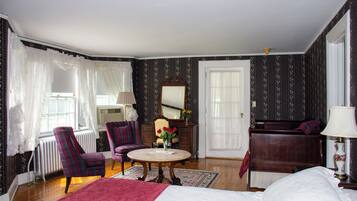 A bedroom with a large bed, a round table with a vase of flowers, a chair, a dresser, and a mirror.