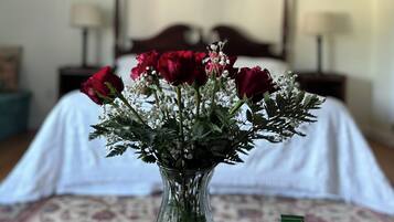 Una habitación con una cama, un jarrón con rosas rojas y un cuenco de vidrio con elementos verdes sobre una mesa.