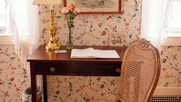 Un escritorio de madera con una lámpara, un florero con flores y un documento en un marco en la pared.