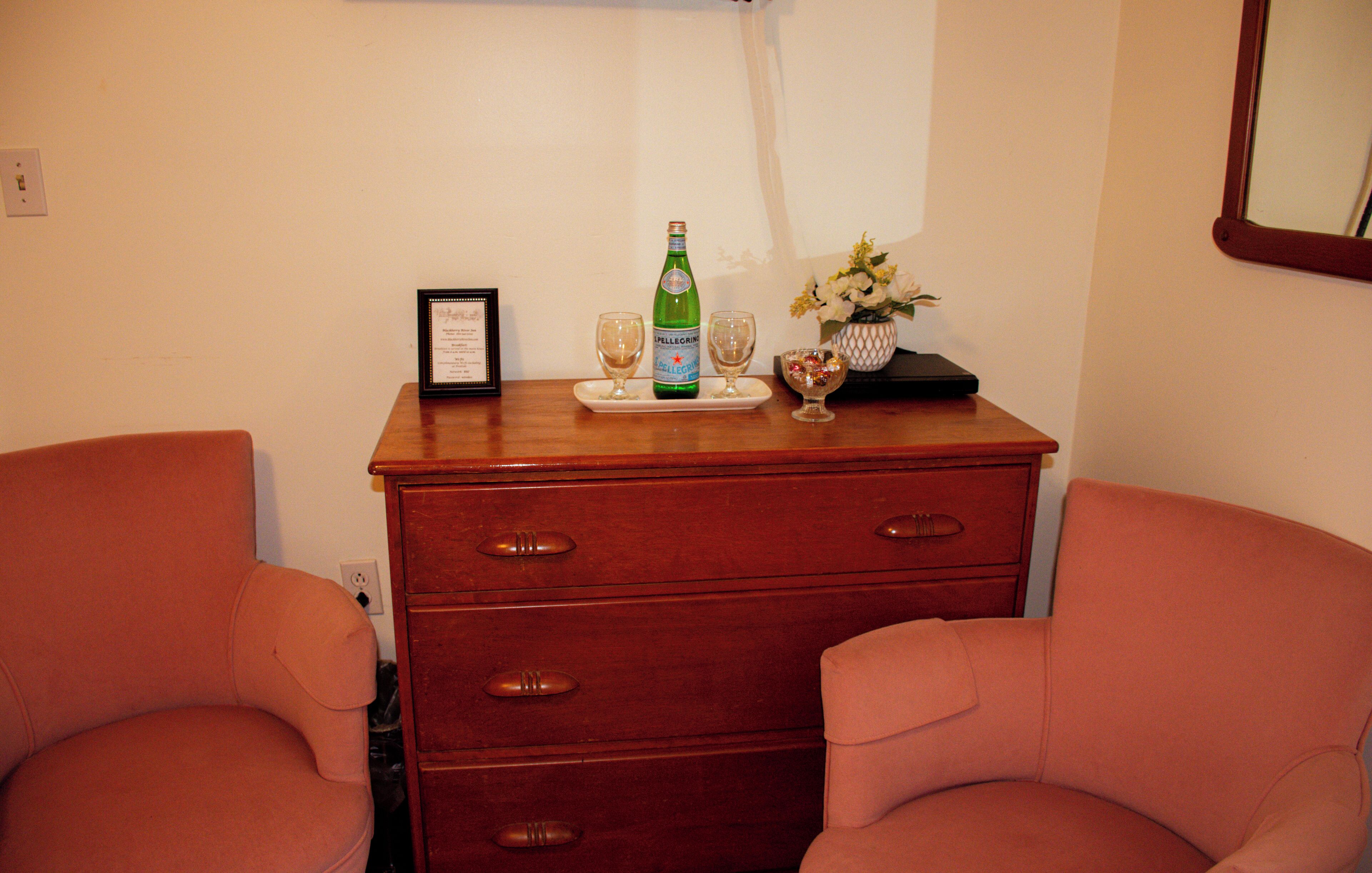 A wooden dresser with drawers, a framed certificate on top, and two glasses on a tray.