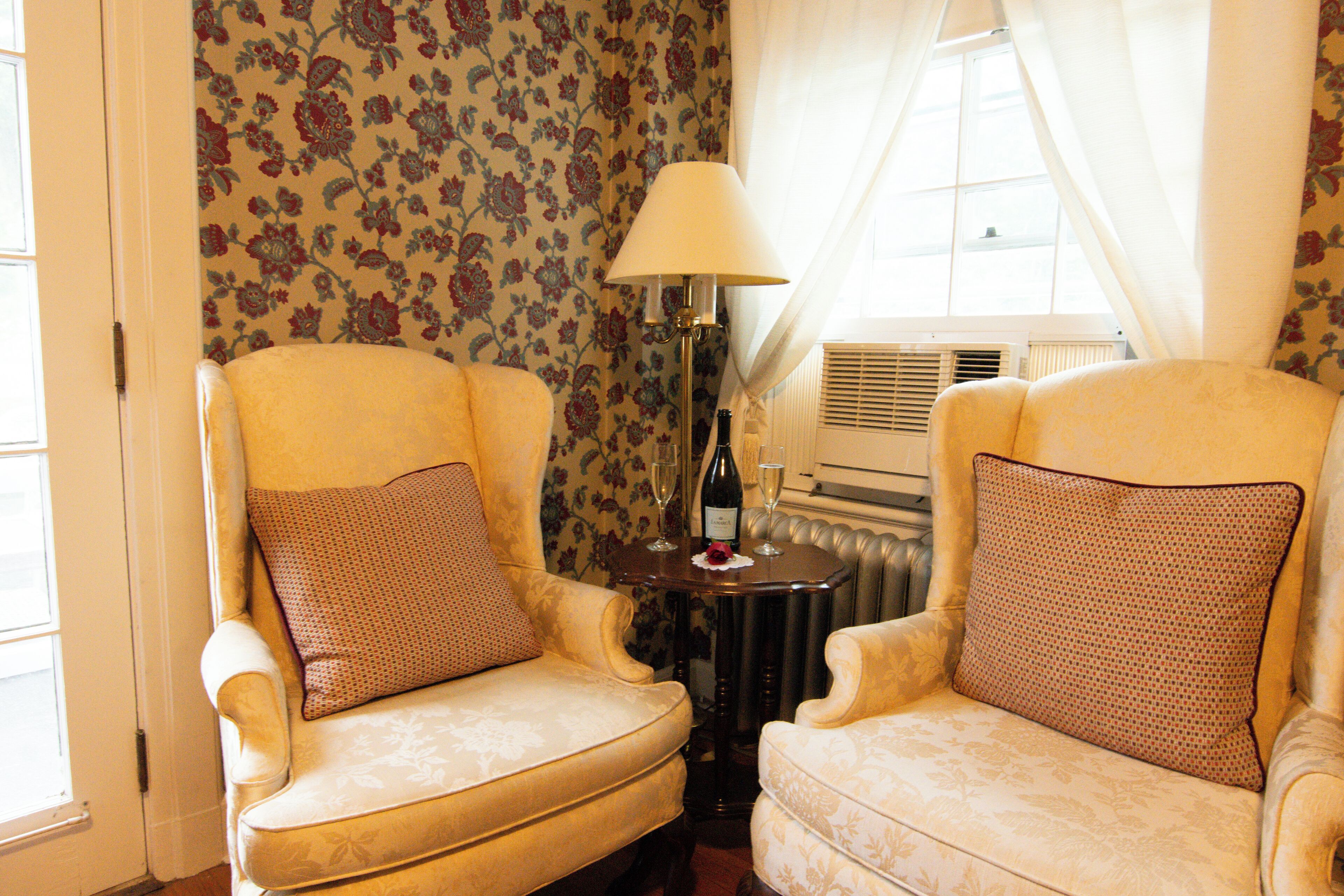 Two armchairs with floral upholstery, a table with a lamp, and a radiator in a room with floral wallpaper.