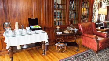 Una habitación con piso de madera, un sillón de cuero rojo, una mesa con mantel blanco y una estantería llena de libros.