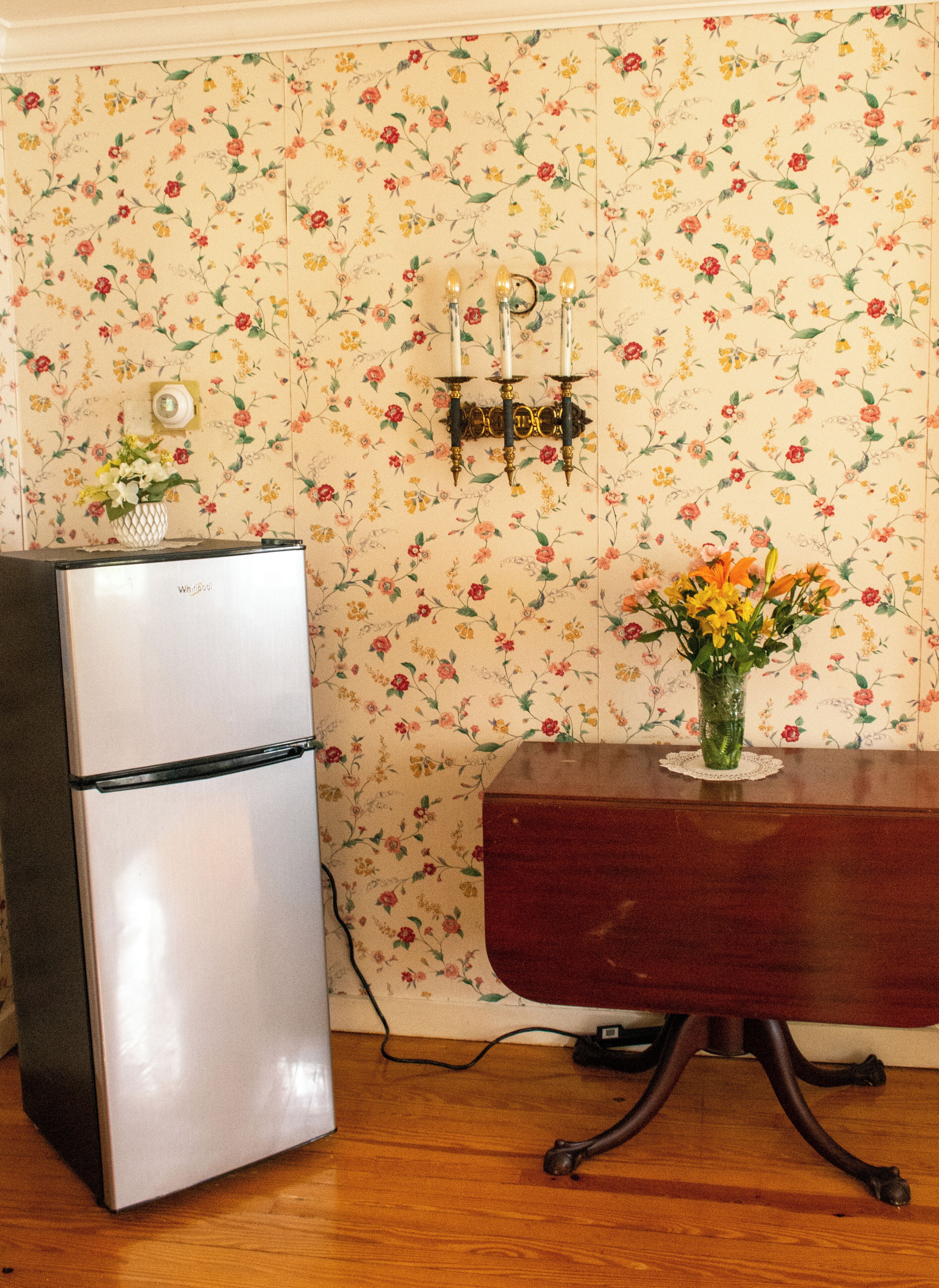 Eine Küche mit Kühlschrank, einem Holzespeisetisch und floraler Tapete.