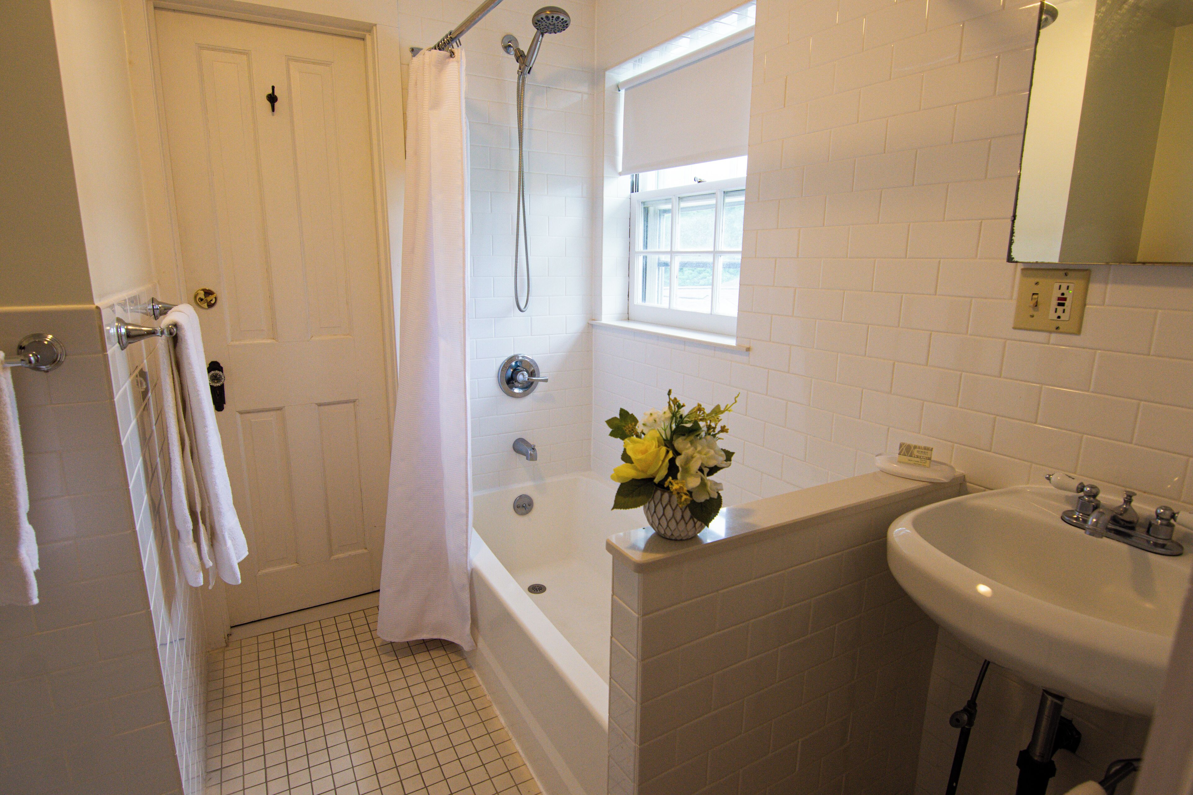 Un bagno con una vasca da bagno bianca, un lavandino e una finestra sopra il lavandino.