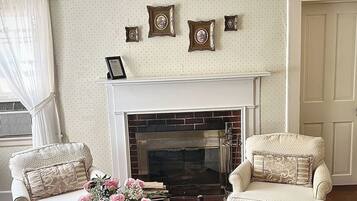 Un salón con chimenea, dos sillones, una mesa baja con un jarrón de flores y una colección de cuadros en la pared.