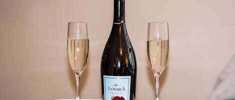 A bottle of Iamarca Prosecco wine, two glasses, a red rose, and two chocolates on a marble table.