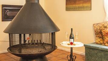 Un estufa de leña con chimenea, una mesita con una botella y vasos, y un sofá con un cojín estampado.