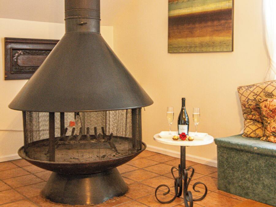 A wood stove with a chimney, a small table with a bottle and glasses, and a couch with a floral cushion.