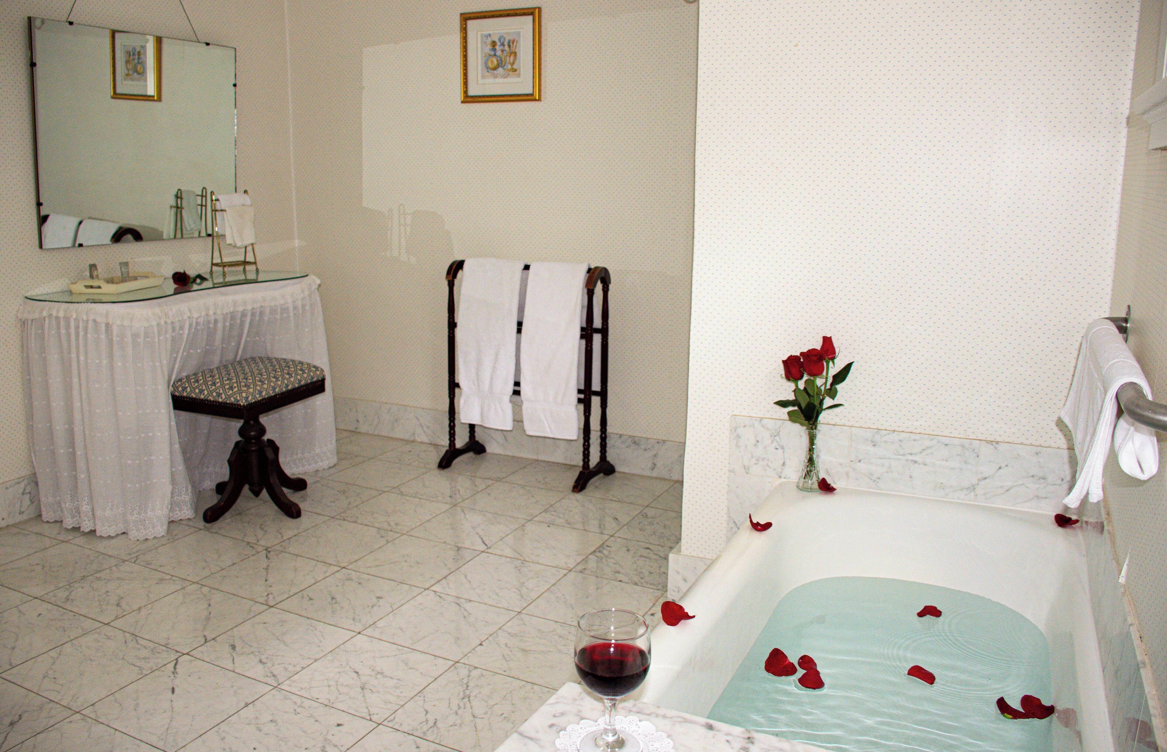 Un baño con bañera, lavamanos, espejo y un florero con rosas rojas.