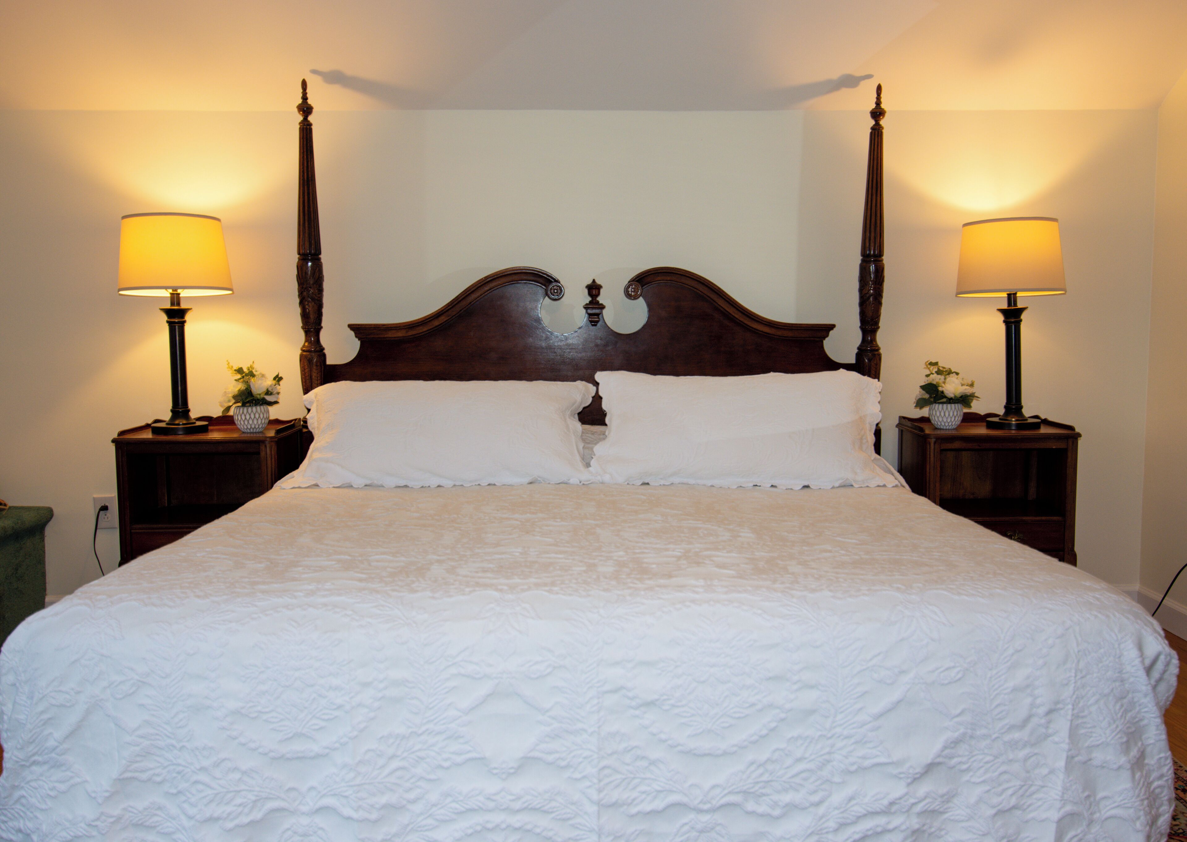 A neatly made bed with a wooden headboard, flanked by two bedside tables with lamps and small flower arrangements.