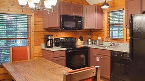 Cocina de cabaña de madera con una mesa de madera, un microondas, una estufa y un refrigerador.