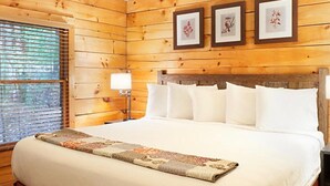 Una habitación con paneles de madera, una cama, ropa de cama blanca y tres cuadros en la pared.