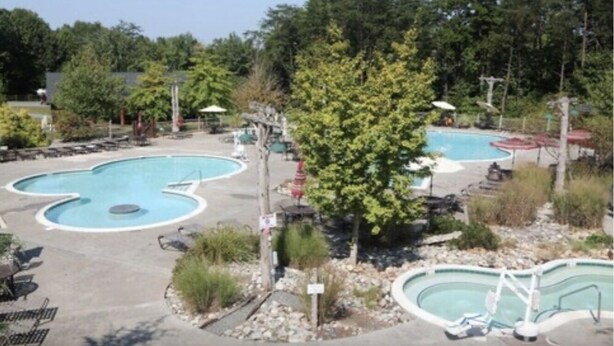Un área de piscina con varias piscinas, sillas de descanso y árboles.