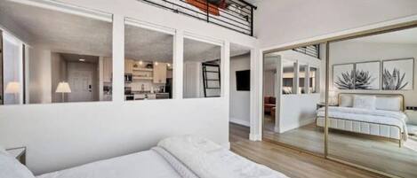 A modern hotel room with a large bed, a balcony with a metal railing, and a view of the interior.