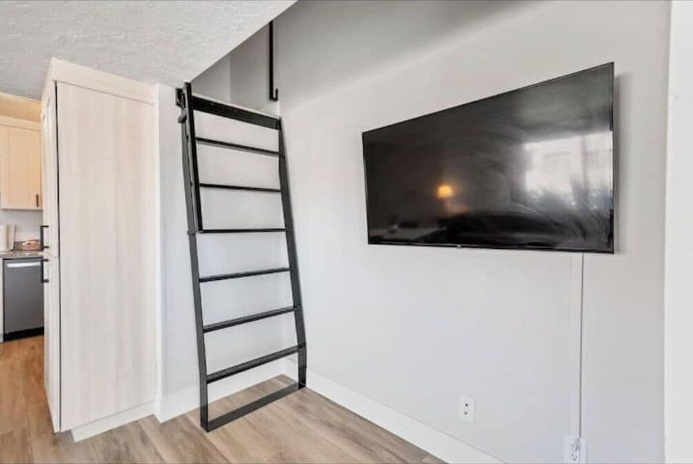 A room with a TV mounted on the wall, a wooden floor, and a door leading to another room.
