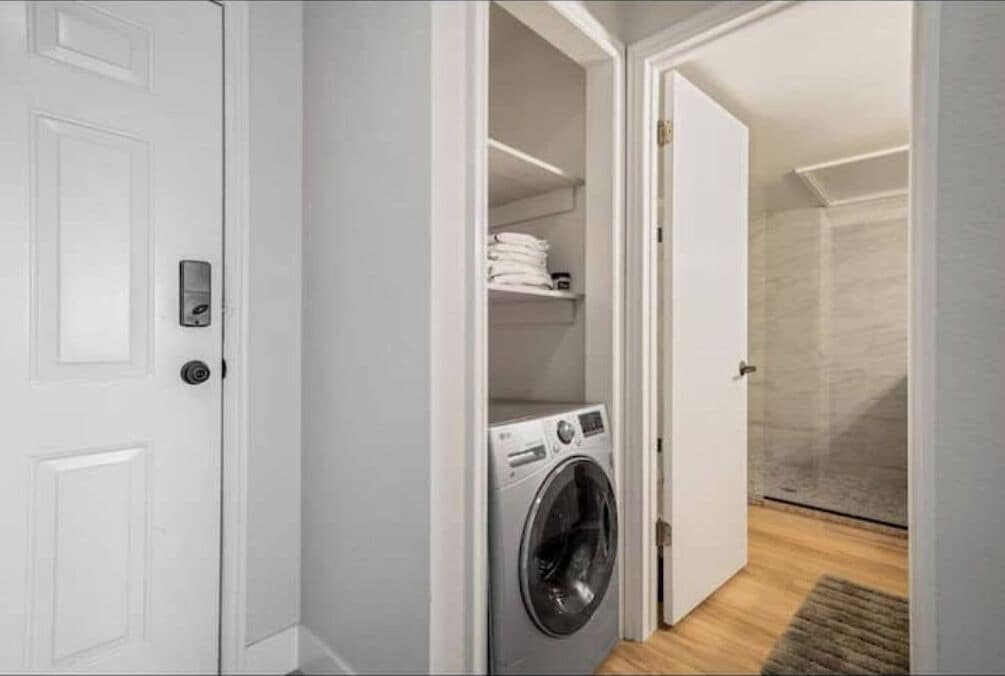 Une buanderie équipée d’un lave-linge, d’étagères où sont pliées les serviettes et d’un espace douche.