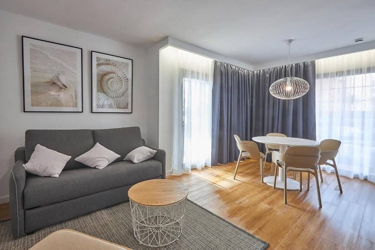 Un salon moderne avec un canapé gris, une table basse ronde et un coin repas comprenant une table et des chaises blanches.
