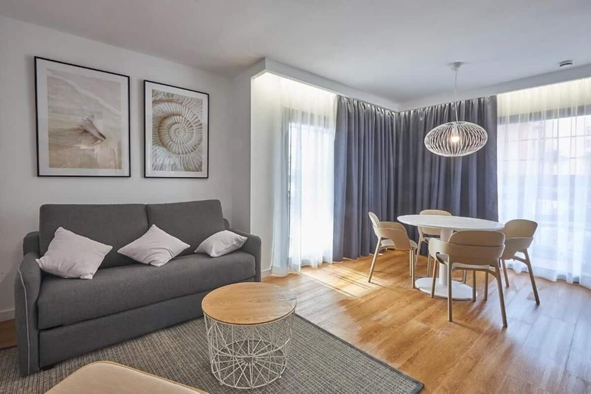 A modern living room with a grey sofa, a round coffee table, and a dining area with a white table and chairs.