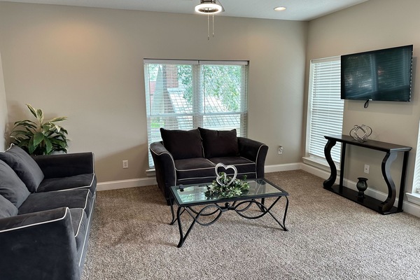 Bright, cozy living room with TV, large windows, and comfy seating