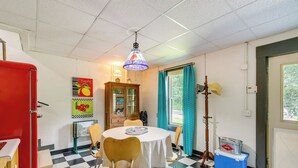 A dining area with a checkered floor, a round table with chairs, a cabinet, and a red refrigerator.