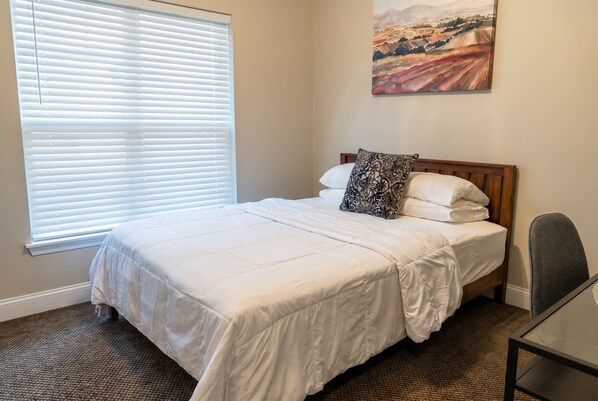 A bedroom with a bed, a window with blinds, a painting on the wall, and a chair. - Top Floor · 3BR 2BA · King Beds · Near Shipyard (Moss Point)