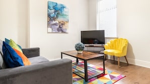 Ein Wohnzimmer mit grauem Sofa, einem gelben Sessel, einem Couchtisch und einem Flachbildfernseher.