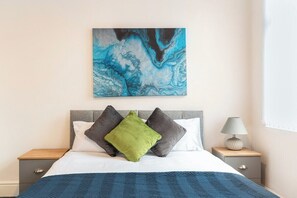 A bedroom with a bed, pillows, a nightstand, a lamp, and a wall art piece.