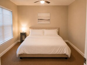 A bedroom with a bed, a ceiling fan, a nightstand, a lamp, and a framed picture on the wall.