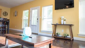 A living room with a wooden coffee table, a TV mounted on the wall, and a door with a window. - Ground Floor Stay · 3BR · Parking · Near Refinery (Moss Point)