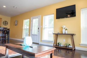 A living room with a wooden coffee table, a TV mounted on the wall, and a door with a window. - Ground Floor Stay · 3BR · Parking · Near Refinery (Moss Point)